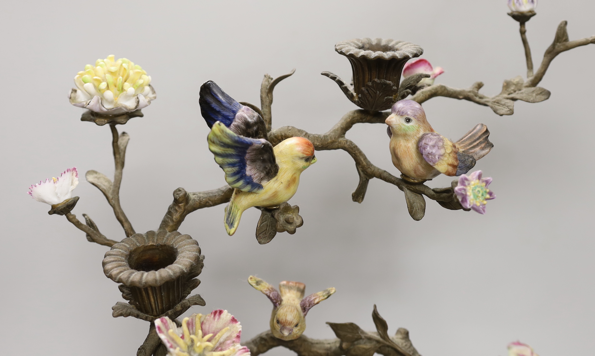 A pair of Victorian style bronzed metal and porcelain three branch candelabra, modelled as birds among branches, each 51cm high